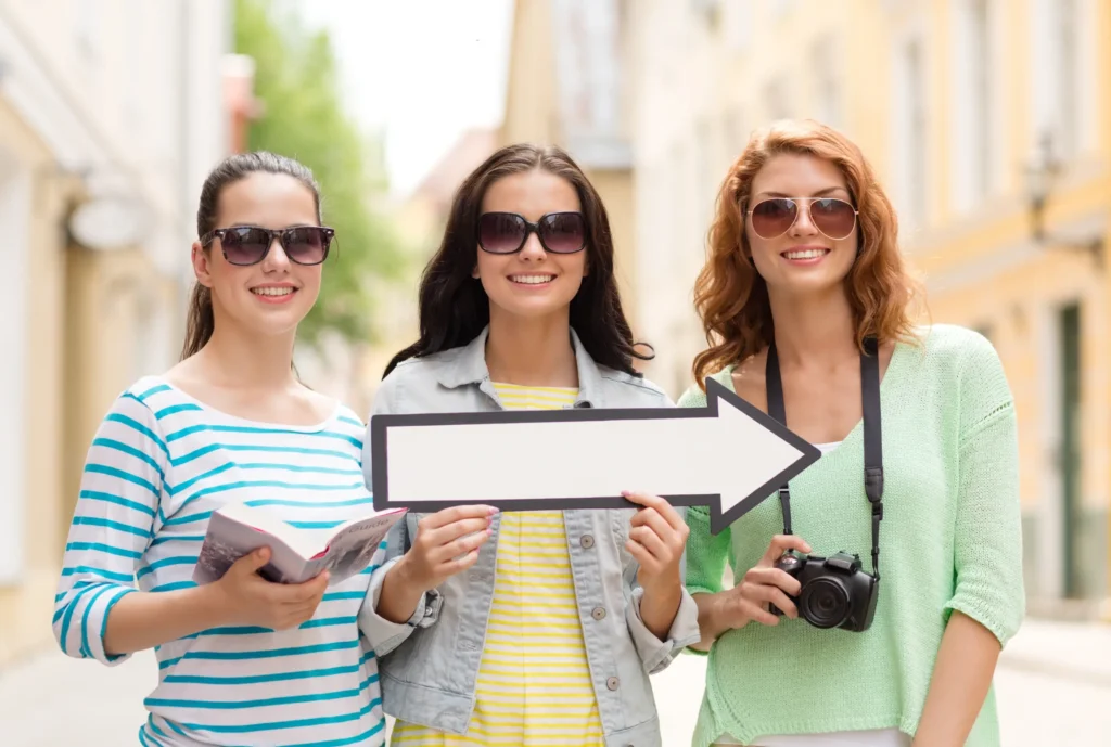 Three young women on a city tour holding a map and a direction sign