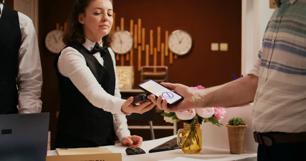 Hotel receptionist processing digital check-in with guest using mobile payment