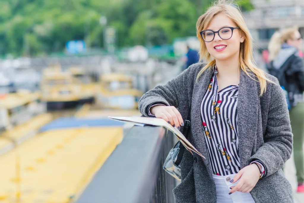 Smiling young woman holding a city map during a guided urban tour by the riverside
