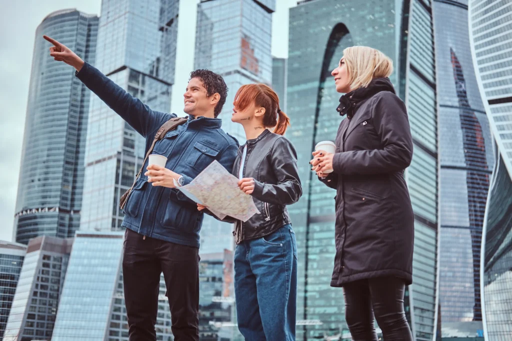 Tour guide showing direction to two female tourists in a modern city with skyscrapers