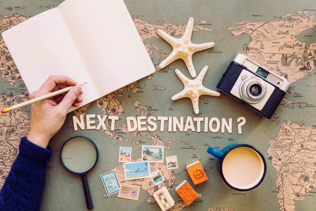 Hand writing in a notebook on a world map with camera, starfish and travel accessories around