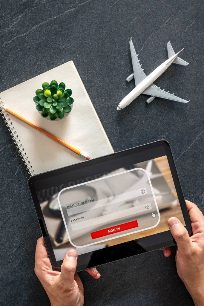 Person holding a tablet and logging into a travel booking app next to airplane model and notebook