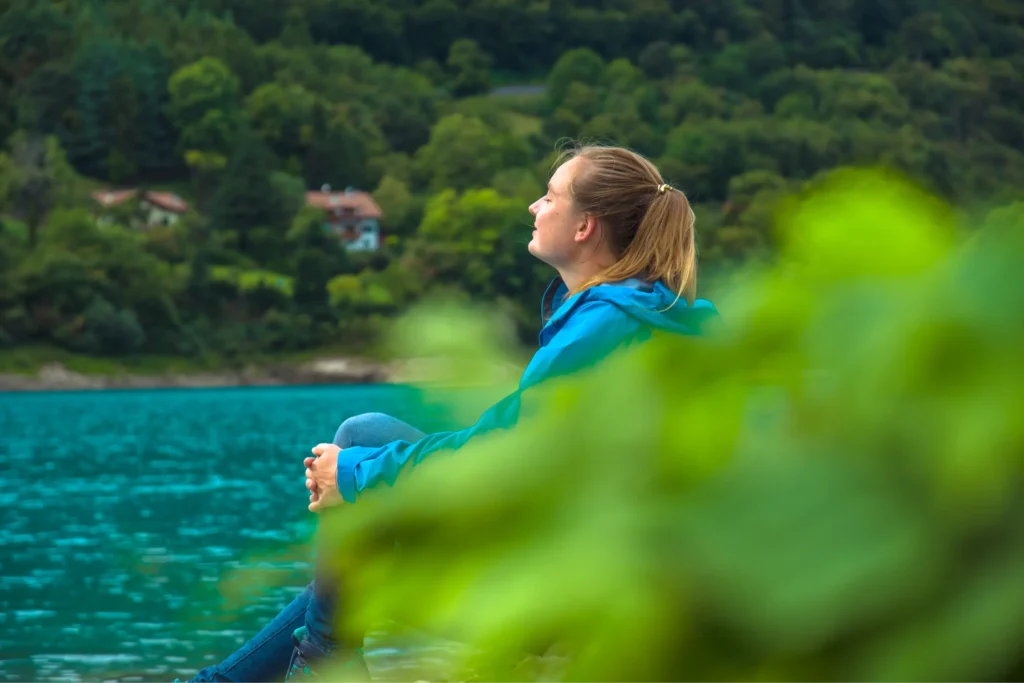Woman relaxing by a mountain lake, enjoying calm eco-tourism and connection with nature.