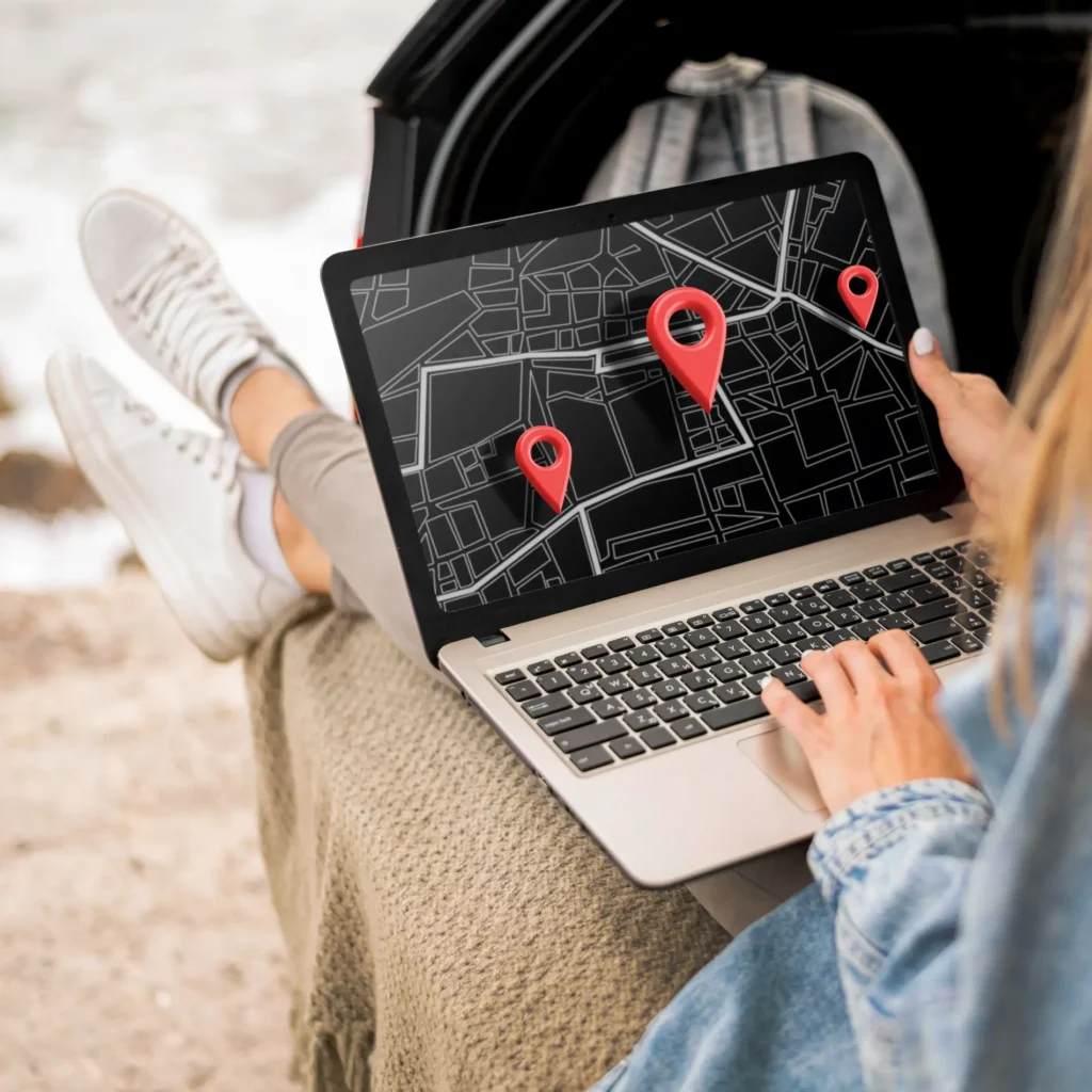 Traveler sitting outdoors with laptop showing location pins — representing local SEO and map-based search for travel businesses