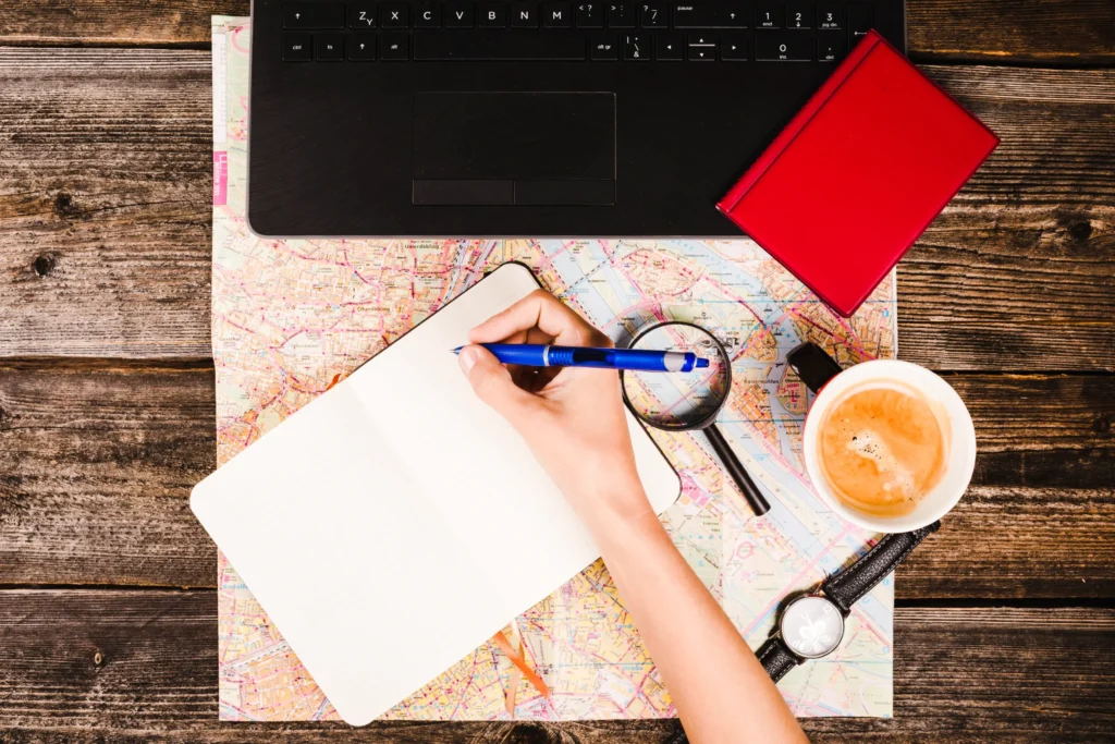 Traveler writing notes on a map with a laptop, symbolizing brand message and content creation for travel agencies.